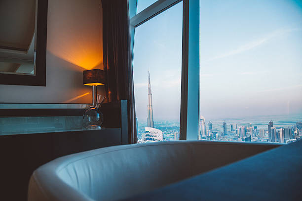 A luxurious room with Dubai skyline, including Burj Khalifa, as seen through a large window at sunset.