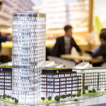 A detailed architectural model of a modern high-rise building with people discussing in the background.