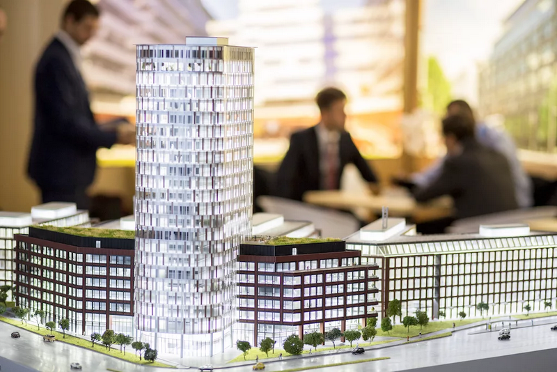 A detailed architectural model of a modern high-rise building with people discussing in the background.