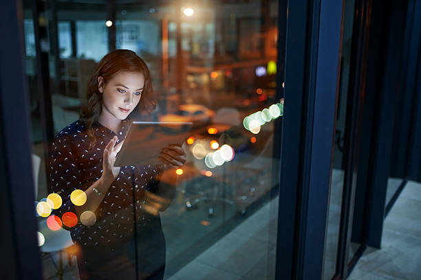 A woman studies mortgage options on a tablet in an evening-lit office, representing UAE mortgage research.