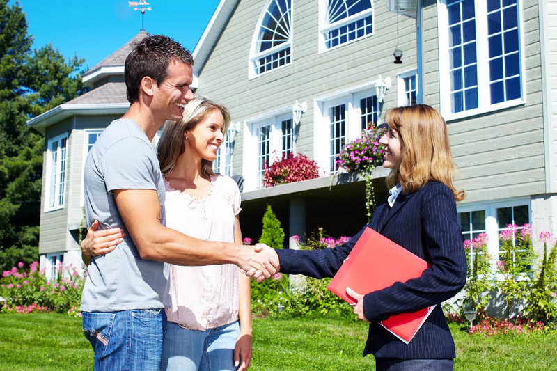 A couple is shaking hands with a real estate agent in front of a large house.